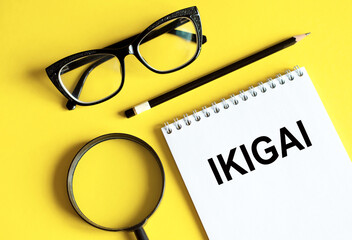 IKIGAI. The word Ikigai on notebook and pencil, magnifier and eyeglasses on yellow background....