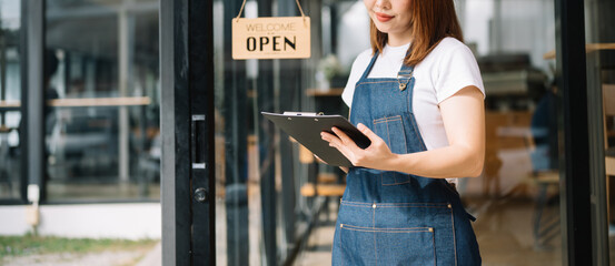 Woman coffee shop owner holding notepad and digital tablet ready to receive orders in cafe restaurant.