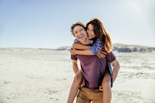 Happy couple piggybacking on sunny beach