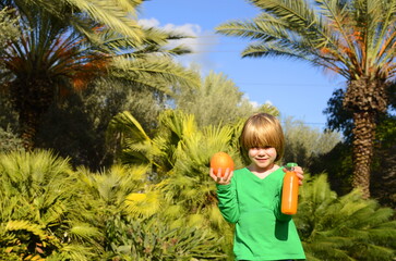 Freshly squeezed orange juice. A boy holds a bottle of orange juice and a fresh orange. Vitamins, baby food, drinks, sweet, harmful, healthy