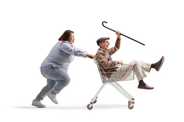 Woman pushing a happy elderly pensioner inside a shopping cart
