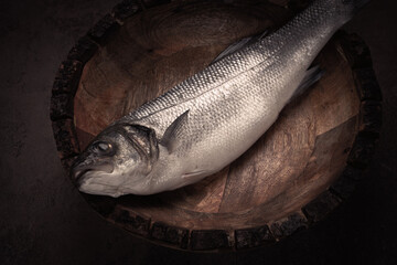 fresh, raw sea bass fish, in a wooden plate, top view, no people.