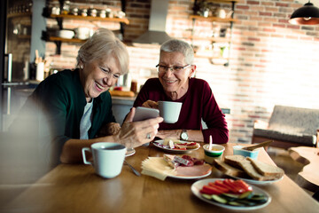 Fototapeta na wymiar Two senior women eating breakfast with a smartphone in the kitchen