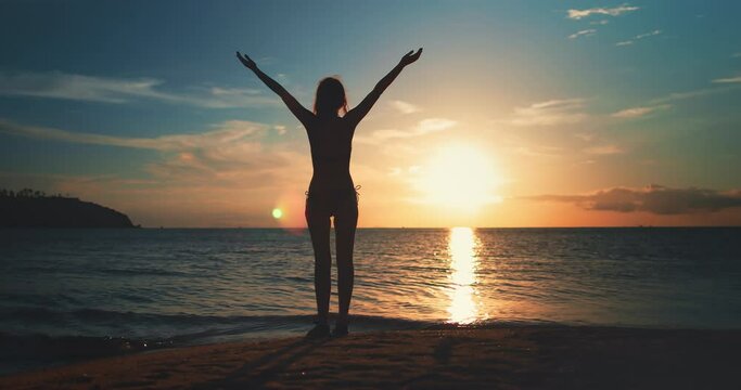 Woman silhouette enjoy ocean bright sunset sky. Female raise hand, colorful clouds and sun. Girl against sunset sky sun backdrop. Watching the sunset with beautiful landscape. Relax vacation travel