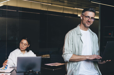 Half length portrait of happy Caucasian male employee in classic eyeglasses smiling at camera...