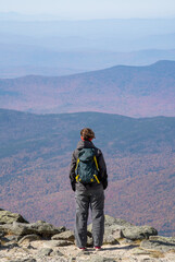 A woman stands on Mount Washington and watches the woods in a distance.