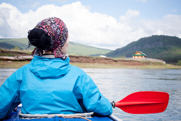 Woman in blue jacket kayaking on river with beautiful landscape of green hills and blue sky