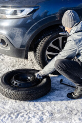 Close up of man replacing flat tyre with spare wheel on snowy road. © zphoto83