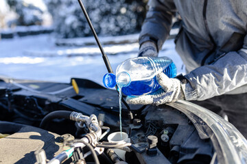 Close up of man hands pouring winter windshield washer fluid into spray tank. - obrazy, fototapety, plakaty
