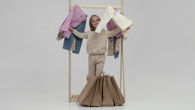 The girl is standing near the closet. Dressing room with clothes on hangers. Newborns, children, toddlers and teens have a wardrobe full of all the clothes. Concept of shopping, clothing advertising.