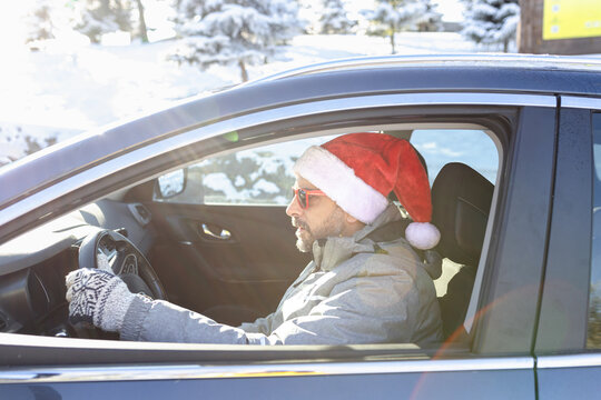 Winter scene of male car driver wearing santa hat and sunglasses.