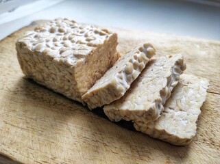 Sliced ​​raw soybean tempeh, a typical Indonesian food on a cutting board.