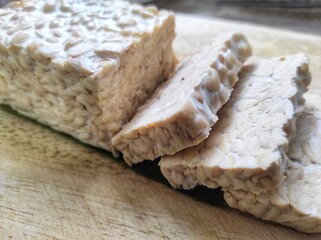 Sliced ​​raw soybean tempeh, a typical Indonesian food on a cutting board.