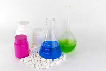Lab glass, drug bottles and pills on white background. Medicine lab, pharmaceutical industry, medicine research. Glass flask and plastic drug bottles and white pills.