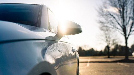 Low angle of a white car with sun shining over the rear view mirror