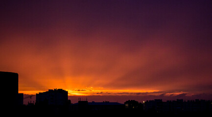 Naklejka premium Vibrant Cityscape at Sunset with Dark Clouds and Warm Glow Behind Tall Buildings