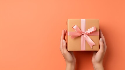 Woman's hands holding a gift in a box with pink bow on peach fuzz background with copy space