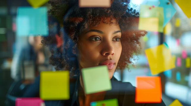 professional woman standing by a glass wall or window covered with colorful post-it notes