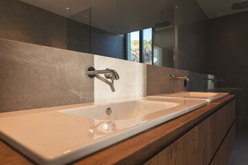 White bathroom sink in a new construction house with gray stone wall and wooden furniture