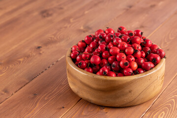 red hawthorn berries in wooden bowl on flat wooden surface.