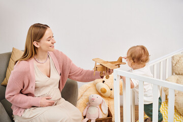 joyful pregnant woman playing with toy plane and little son n nursery room at home, happy motherhood