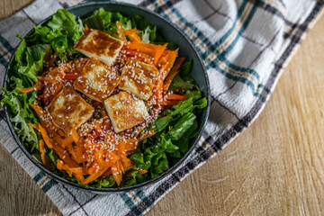 green salad with greek pan fried cheese served on wooden background with kitchen cloth textile napkin