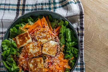 green salad with greek pan fried cheese served on wooden background with kitchen cloth textile napkin