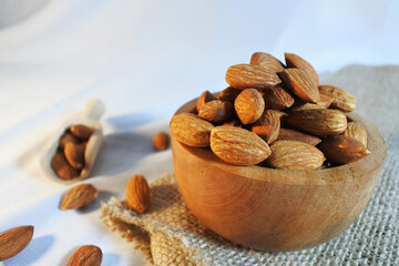Almond nuts in wooden bowl on white fabric background. Healthy food.