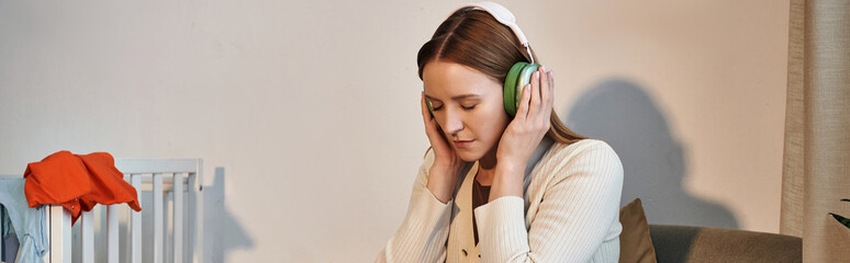 Naklejka premium grieving woman trying to relax by listening music in headphones in dark nursery room, banner