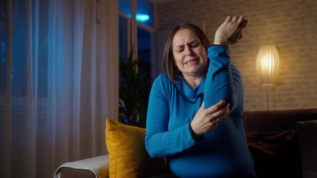 Mature woman with arm pain. Old female massaging painful hand indoors. Old woman hand holding her elbow suffering from elbow pain. Unhappy woman suffering from pain in hand at home. 