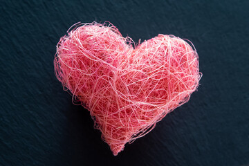 Pink fabric heart shape over black nature background.