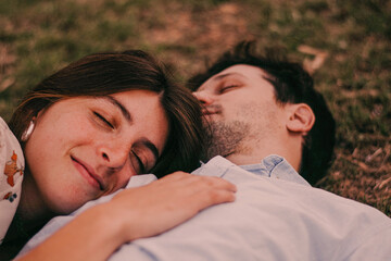 Obraz premium Happy, smiling couple in a green park with the sunset light, hugging, kissing, walking hand in hand, and lying on the ground and grass, representing their love outdoors and sincere love