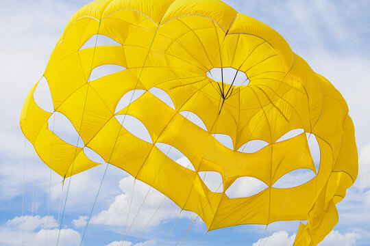 Bright yellow parachute with smile on sky with clouds background. Concept of extreme sport, adventure, challenge, relaxation