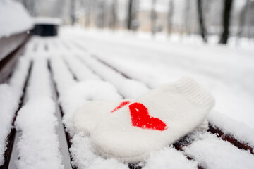 Warm white mittens with a heart on a snow-covered bench in a winter park,a place for text