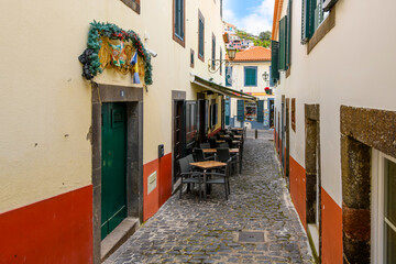 A narrow alley with a sidewalk cafe in the old town center of the Portuguese fishing village of Câmara de Lobos, Portugal, on the Canary Island of Madeira.
