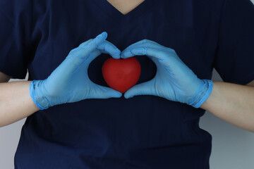 Health care professional wearing surgical scrubs holding a red plastic heartiness the hands. Red month concept for taking care of the heart 