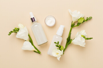 Obraz na płótnie Canvas Facial cosmetic products with freesia flowers on color background, top view