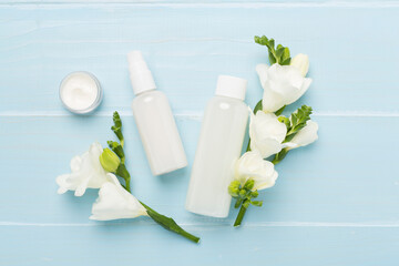 Facial cosmetic products with freesia flowers on wooden background, top view