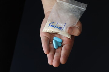Woman holding a pack with fentanyl powder and pills to illustrate the drug addiction 