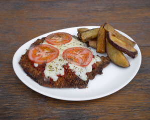 Traditional Argentinian dish. closeup view of a fried breaded meat steak, called Milanesa Napolitana, with mozzarella cheese, tomato and oregano, with fried sweet potatoes, in a white dish.