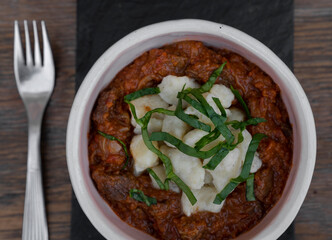 Top view of traditional Hungarian dish, goulash stew with veal and gnocchi, in a black dish on the restaurant wooden table.	
