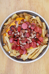 Fries. Top view of fried potatoes with sliced sausages and crispy bacon, in a metal dish with a wooden background.	