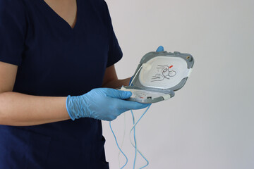 Health care professional wearing gloves holding a defibrillator pad in the hands. Copy space in the right side - obrazy, fototapety, plakaty