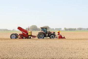 a tractor with a potato planter is planting potatoes in a field in springtime in the dutch countryside