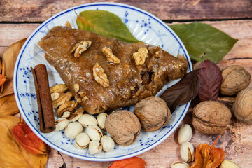 Turkish Baklava sweet cake on the plate, decorated with fresh pistachios, nuts, vanilla and dry autumn leaves, on wooden massive table  