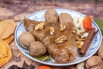 Turkish Baklava sweet cake on the plate, decorated with fresh pistachios, nuts, vanilla and dry autumn leaves, on wooden massive table  