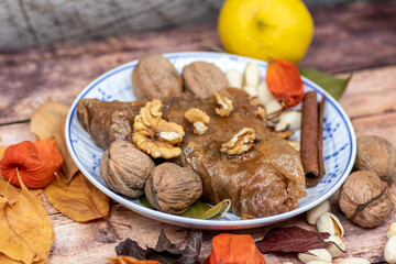 Fototapeta premium Turkish Baklava sweet cake on the plate, decorated with fresh pistachios, nuts, vanilla and dry autumn leaves, on wooden massive table 