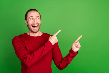 Portrait of ecstatic guy with long hair wear red shirt directing look at impressive offer empty space isolated on green color background