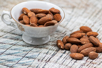 Close up roasted organic brown almond seed on wooden table and some of almond in white decorative porcelain cup