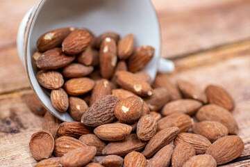 Close up roasted organic brown almond seed on wooden table and some of almond in white decorative porcelain cup